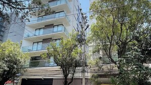 A multi-story building with a garage entrance, two parked cars, and overhead power lines. - Loft Estudio Cdmx Alberca y Gym / Smart Penthouse (Ciudad de México)