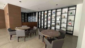 A modern lounge area with two round tables and chairs, a bookshelf with various items, and a wooden accent wall. - Loft Estudio Cdmx Alberca y Gym / Smart Penthouse (Ciudad de México)