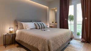 Une chambre avec un grand lit, une table de chevet avec une lampe, un miroir et une vue sur la verdure à l’extérieur.