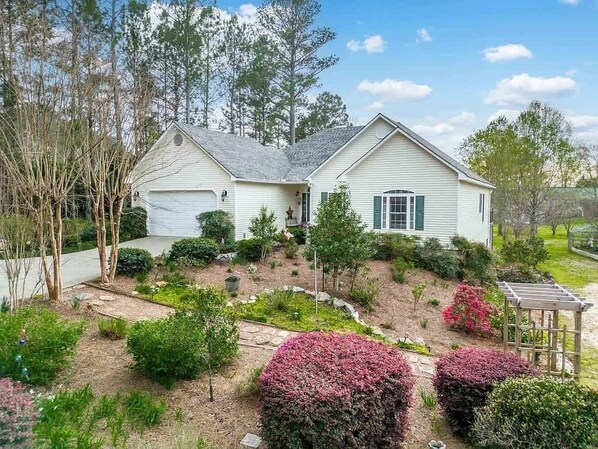A two-story house with a garage, surrounded by a landscaped garden with various shrubs and a pergola. - Sleeps 14, Game Room,Movie Theater,Dock +MORE (Eatonton)