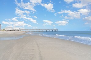 En strand med en brygga som sträcker sig ut i vattnet, en sandstrand och en klar himmel.