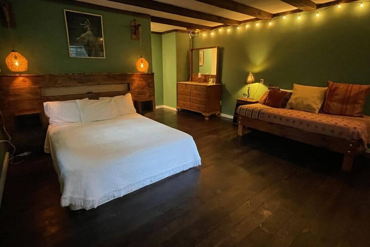 A bedroom with a large bed, a smaller sofa, a dresser, and a mirror.