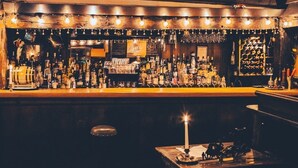 A bar with a variety of bottles and glasses on shelves, a candle on a table, and a brick wall in the background. - Race Brook Lodge  (Sheffield)