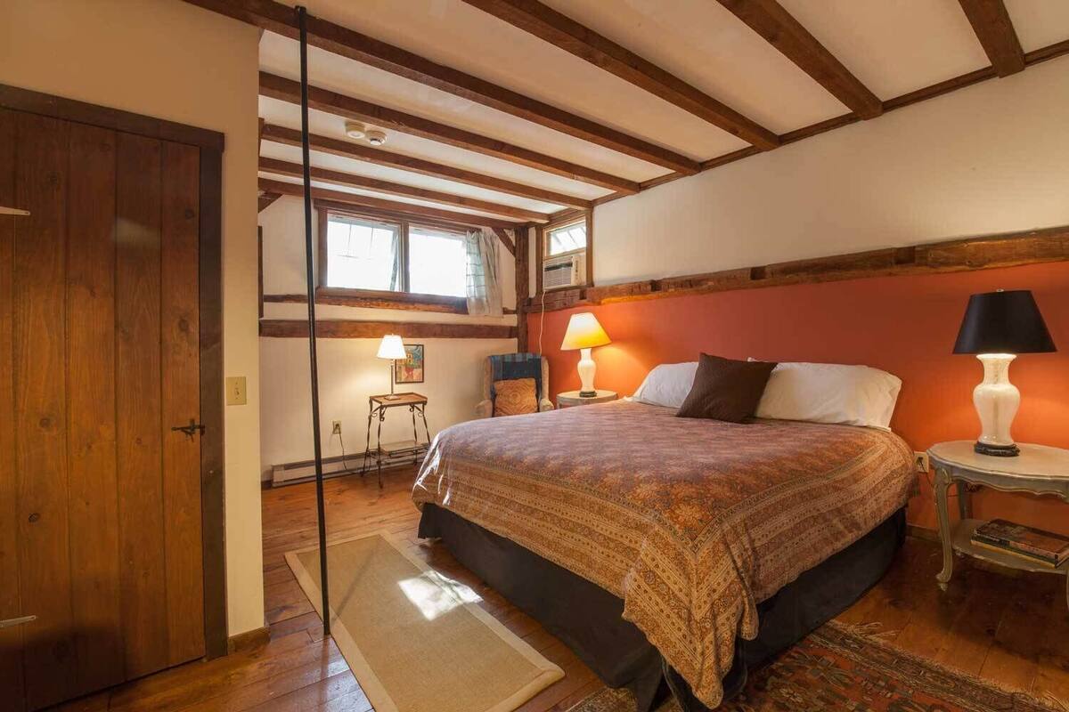 A bedroom with a large bed, two bedside lamps, a wooden door, and a window with curtains.