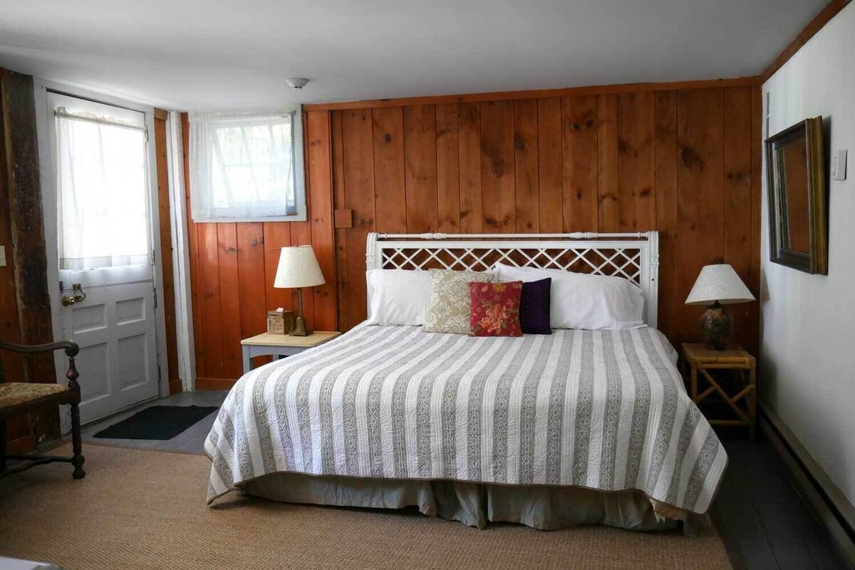 A bedroom with a wooden paneled wall, a bed with a white headboard, two bedside tables with lamps, and a chair.