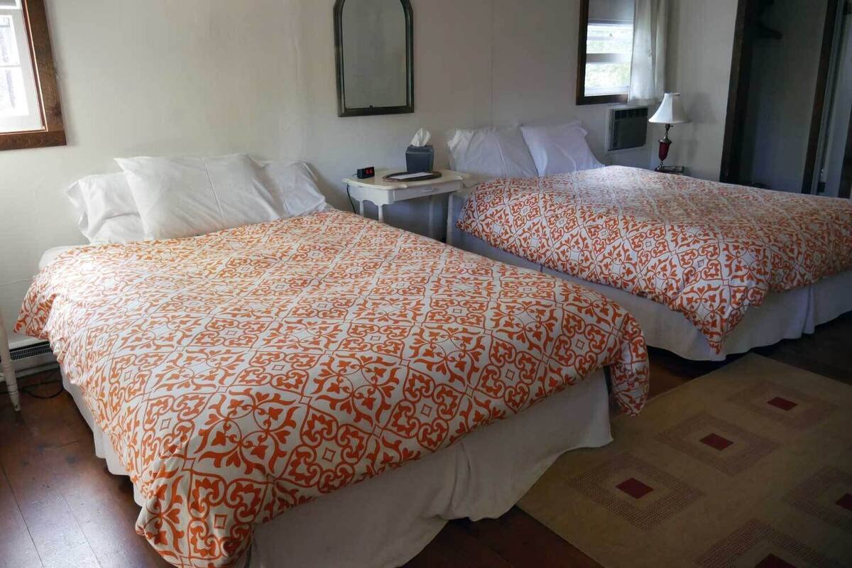 Two beds with matching orange and white patterned bedspreads, a bedside table with a lamp, and a mirror on the wall.