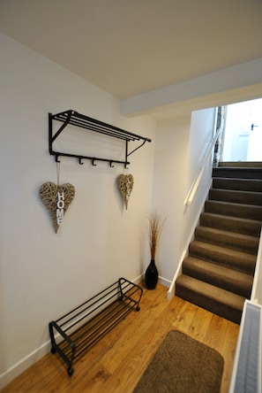 Staircase leads to a cozy living space with a decorative metal rack and a vase with dried plants.