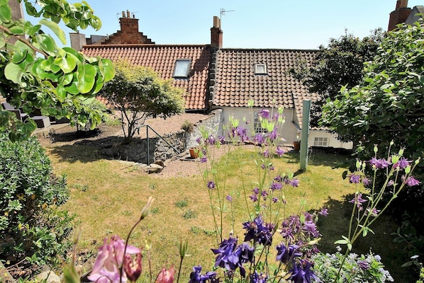 Set amidst a beautifully maintained garden, this charming property boasts a traditional red-tiled roof and a stone wall.
