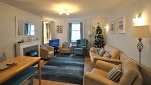 A living room with a fireplace, a television, a Christmas tree, and a sofa. - The Cottage by the Harbour, St Monans (Saint Monans)
