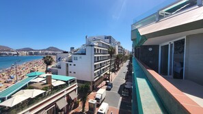 Ein Hotel mit Dachterrasse, Blick auf den Strand, einem Parkplatz sowie eine Fernsicht auf Meer und Berge.