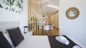 Una habitación de hotel moderna con cama, un escritorio pequeño, una zona de comedor y una cocina al fondo.