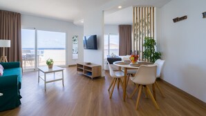 Un salón moderno con un sofá, una mesa de comedor con sillas, un televisor montado en la pared y un balcón con vistas.