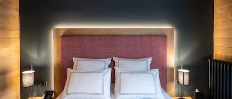 A modern hotel room with a large bed, two bedside tables, a red patterned headboard, and a wooden ceiling.