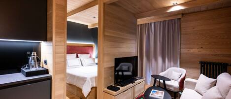 A modern hotel room with a wooden ceiling, a bed with white bedding, a small desk with a lamp, a sofa, and a red and black patterned rug.