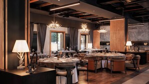 A modern dining area with multiple tables, chandeliers, and a wooden accent wall.