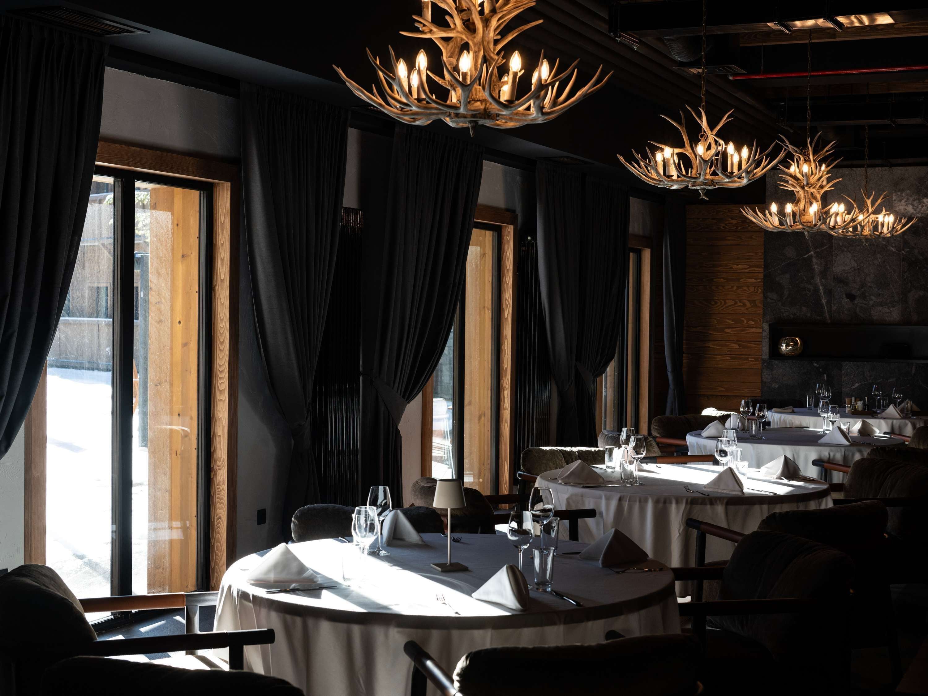 Een restaurant met ronde tafels, donkere gordijnen en kroonluchters.