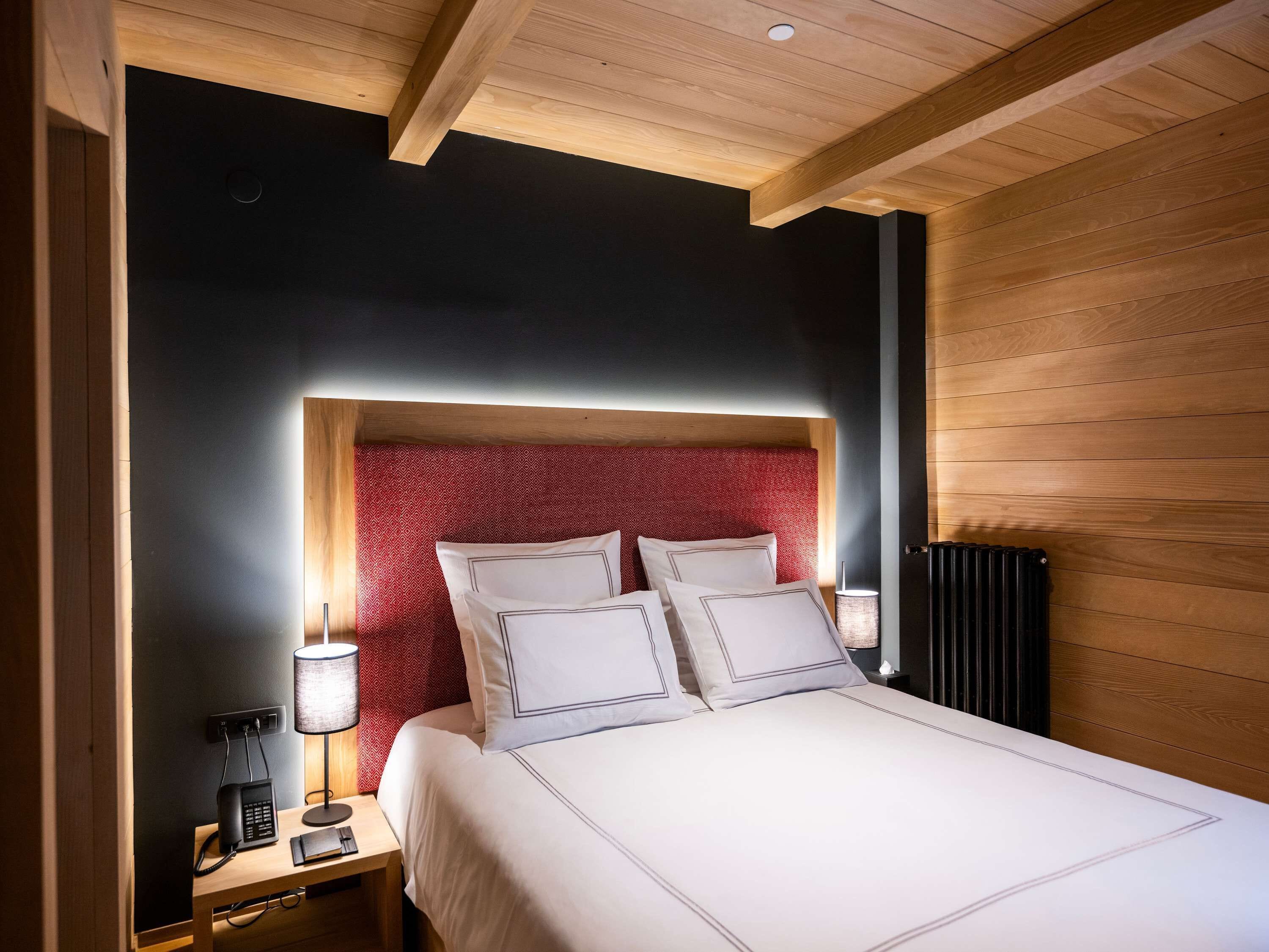 A modern bedroom with a wooden ceiling, a red patterned headboard, and a bedside table with a lamp and phone.