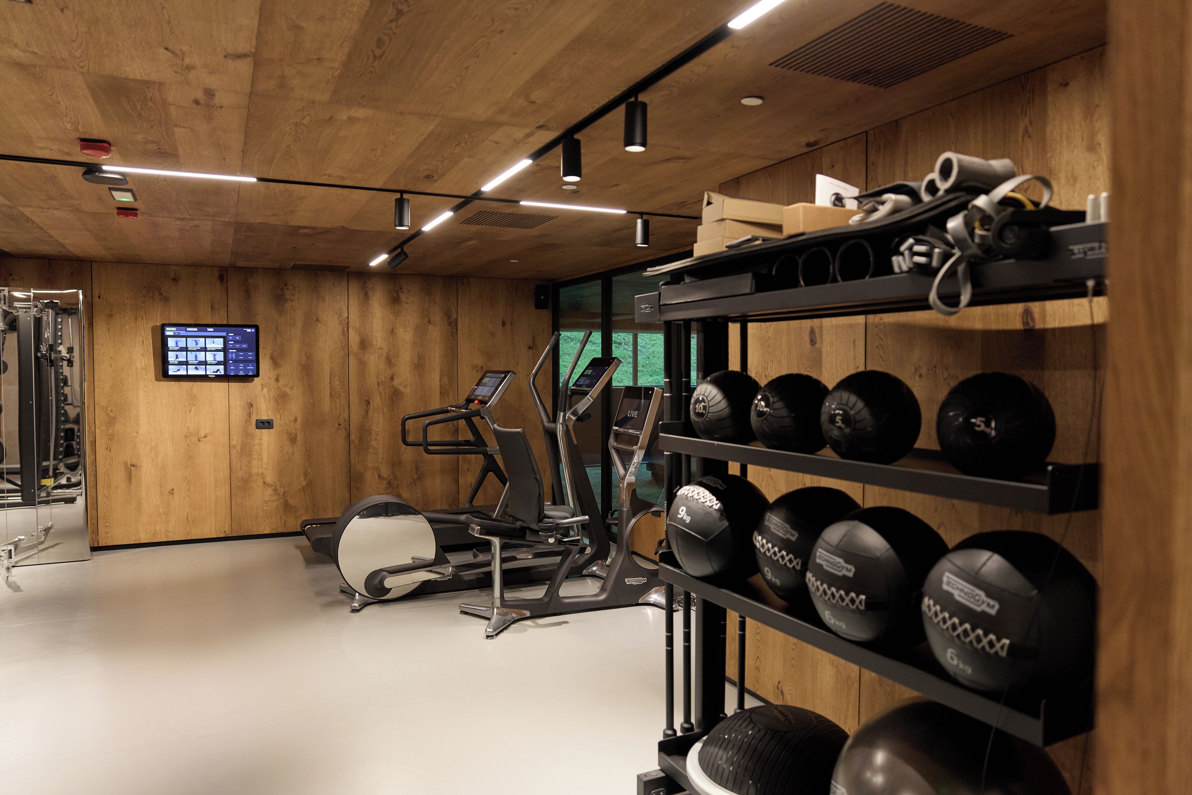 Una palestra con attrezzature da allenamento, un display digitale e uno scaffale a parete con palle da ginnastica.