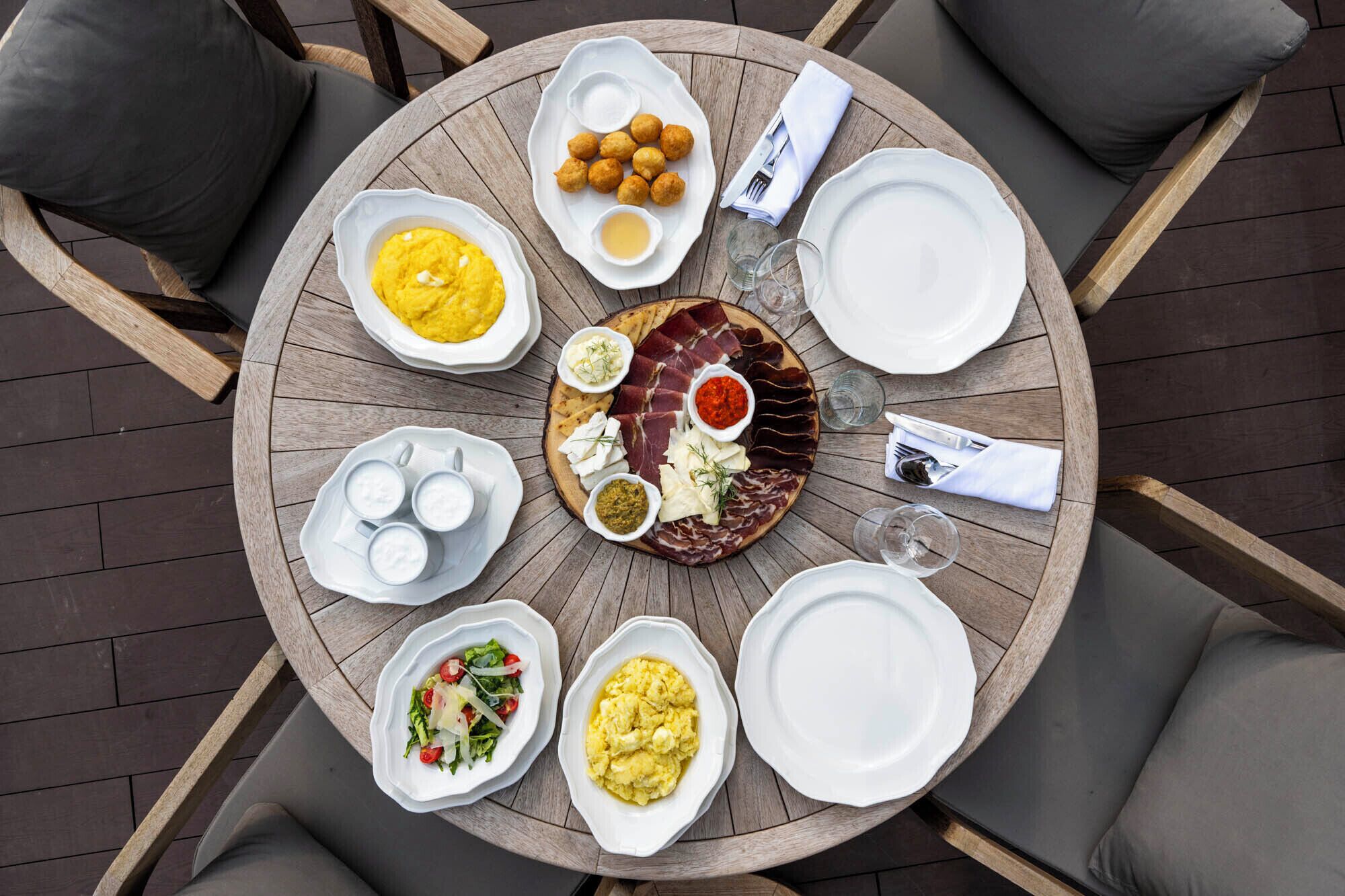 A round wooden table with various dishes and plates, surrounded by chairs.
