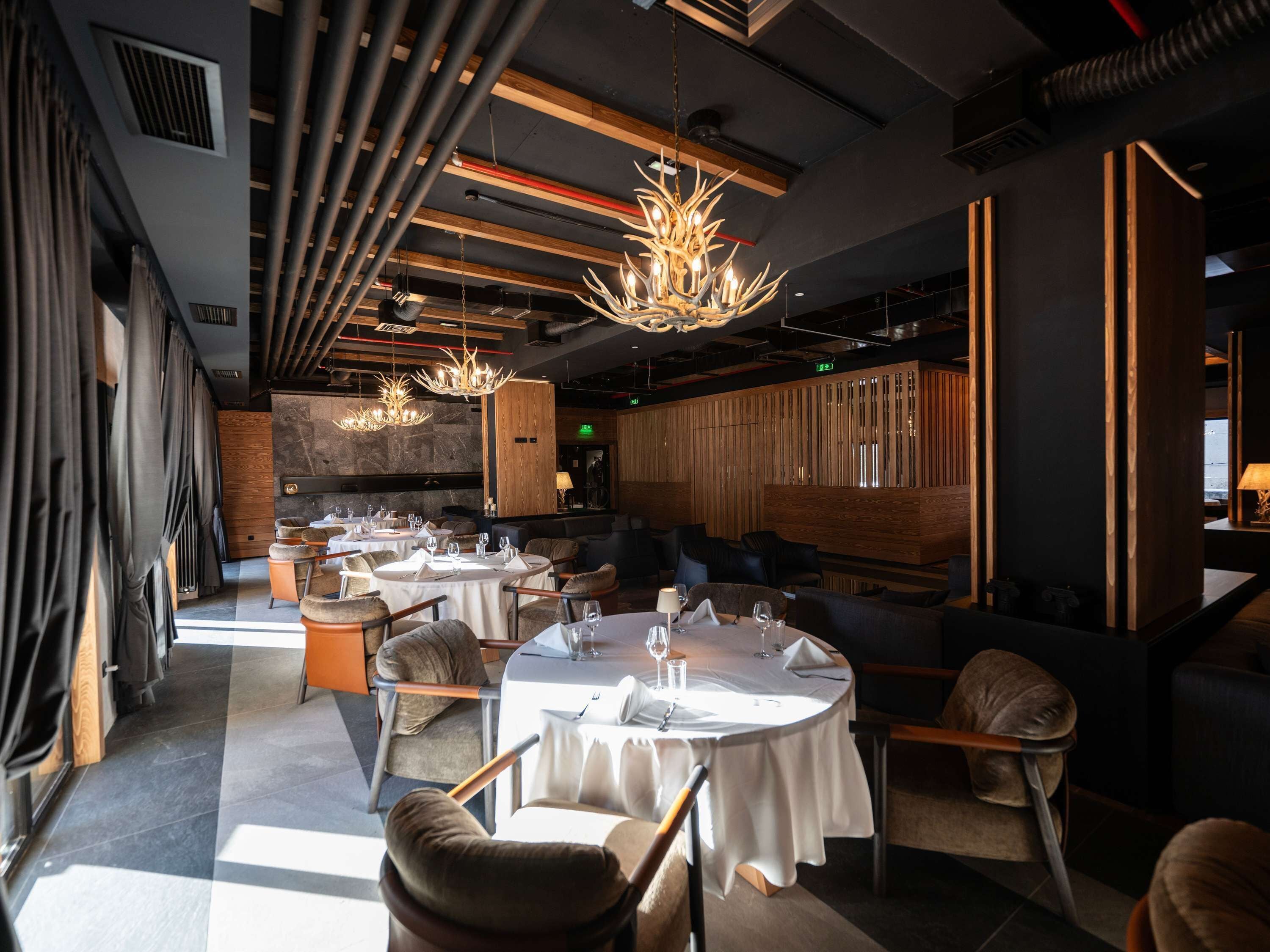 A modern restaurant with round tables, comfortable seating, and a stylish chandelier.
