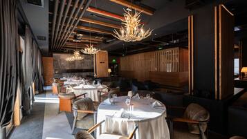 A modern restaurant with round tables, comfortable seating, and a stylish chandelier.