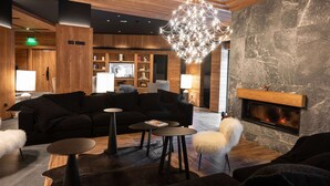 A modern living room with a fireplace, dark sofas, and a chandelier.