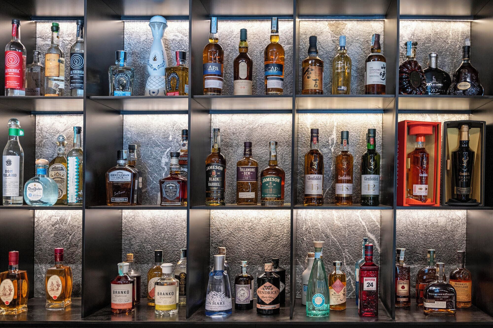 Una pared con una variedad de botellas de licores exhibidas de forma ordenada.