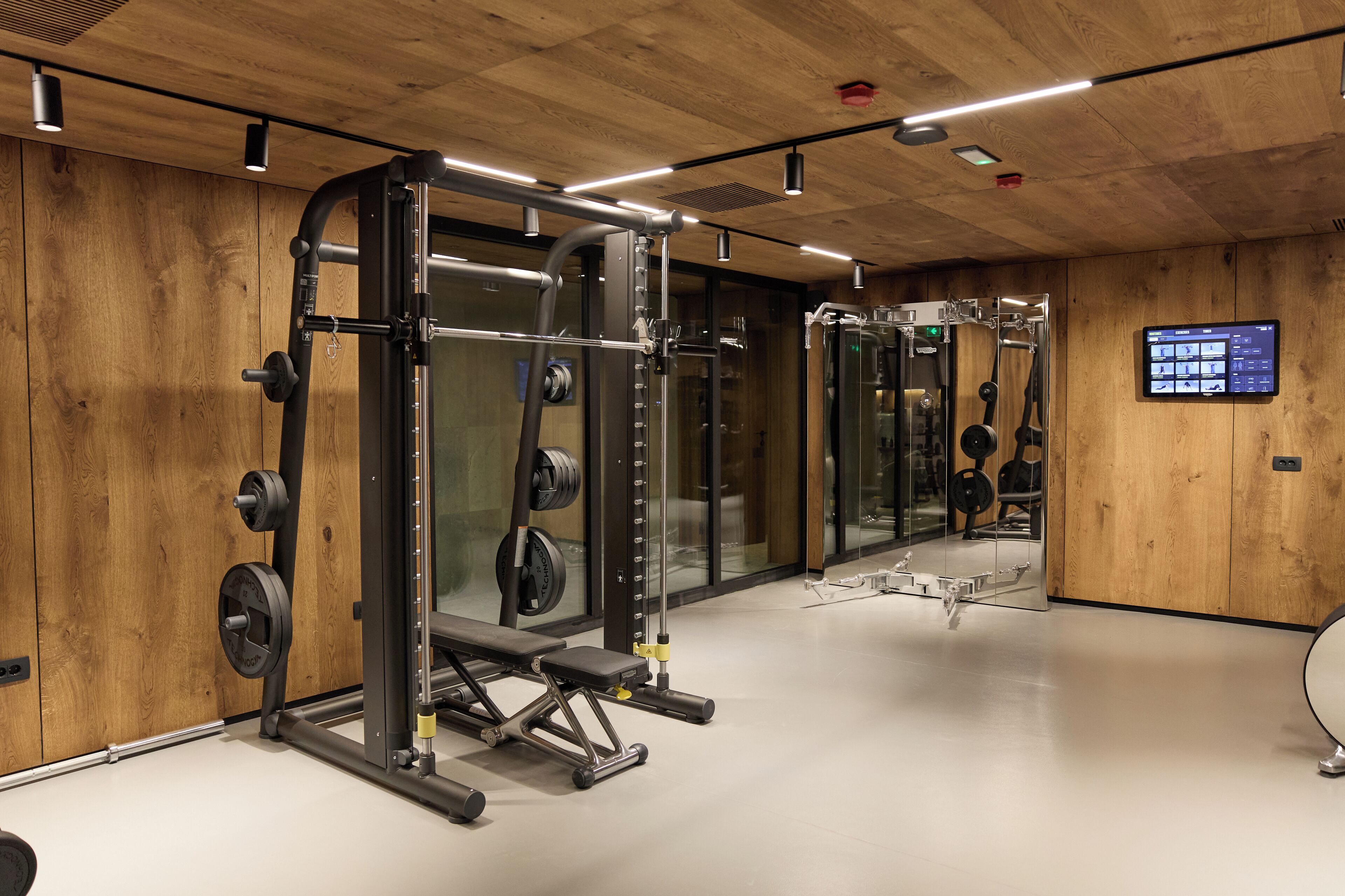 Ett gym med utrustning för styrketräning, en digital skärm och väggar av trä.