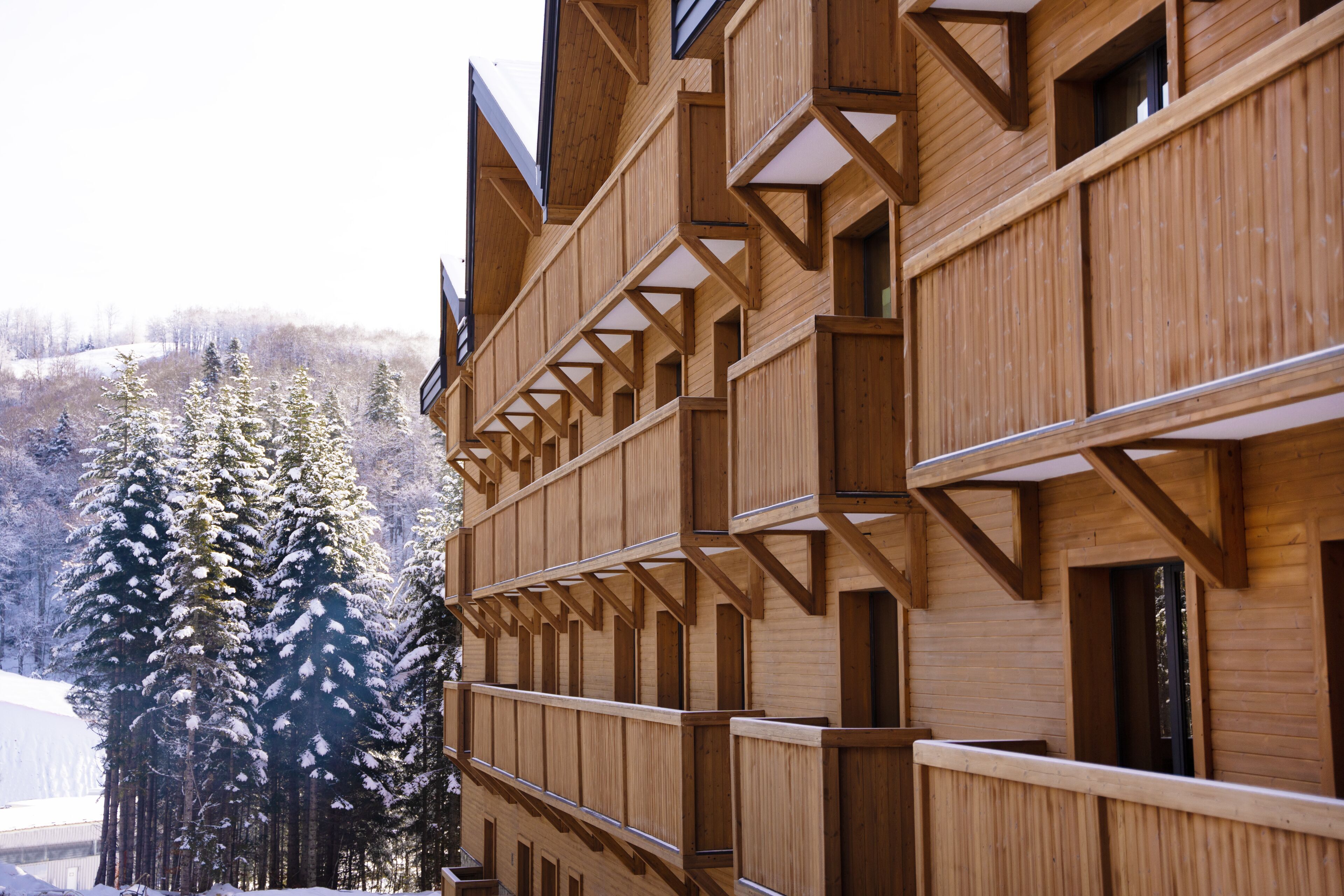 A wooden building with multiple balconies and windows, surrounded by snow-covered trees.