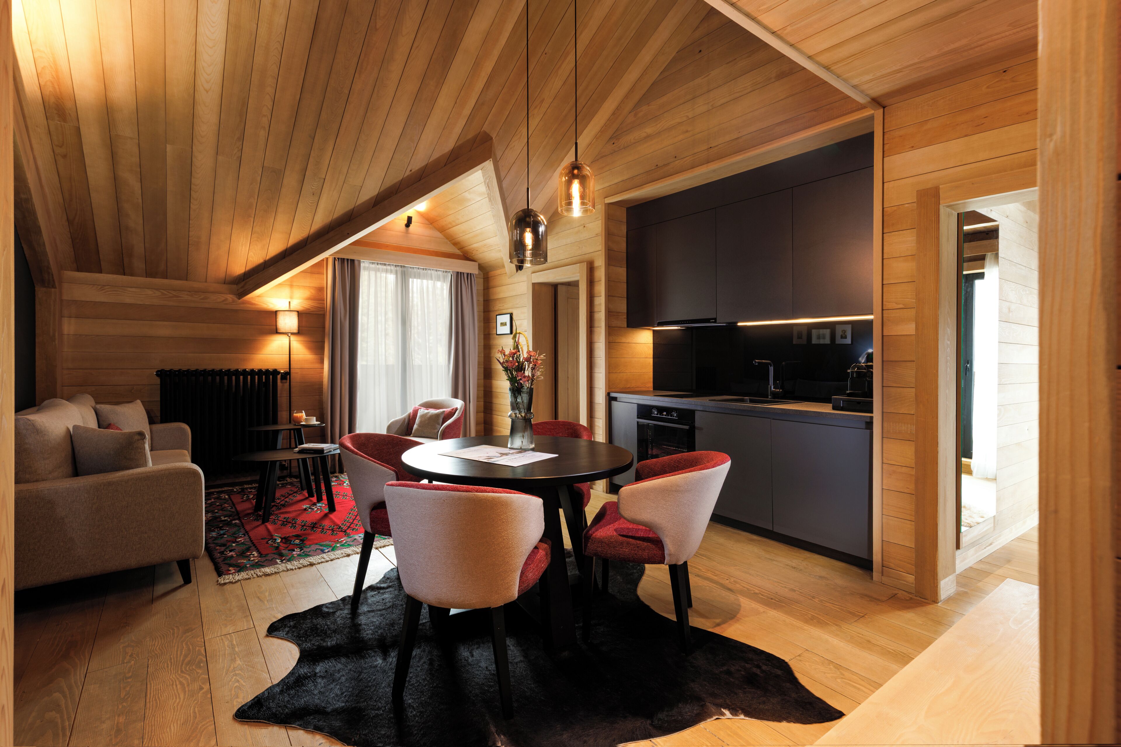 A modern interior with a dining area, kitchen, and living space, featuring wooden ceilings and a black rug.