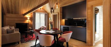 A modern interior with a dining area, kitchen, and living space, featuring wooden ceilings and a black rug.