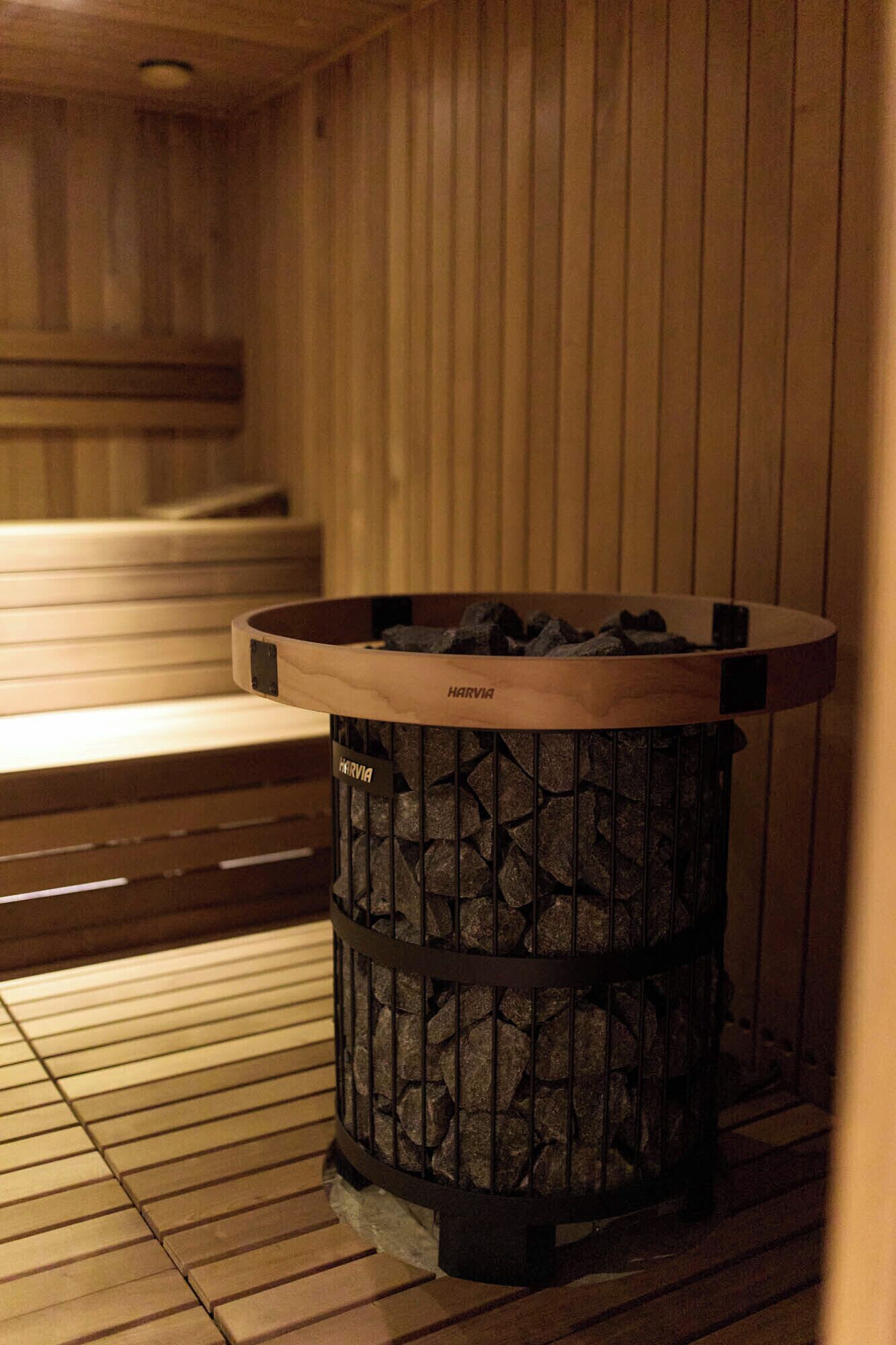 Eine Sauna mit einem Harvia Holzofen, Holzbänken und einem gefliesten Boden.