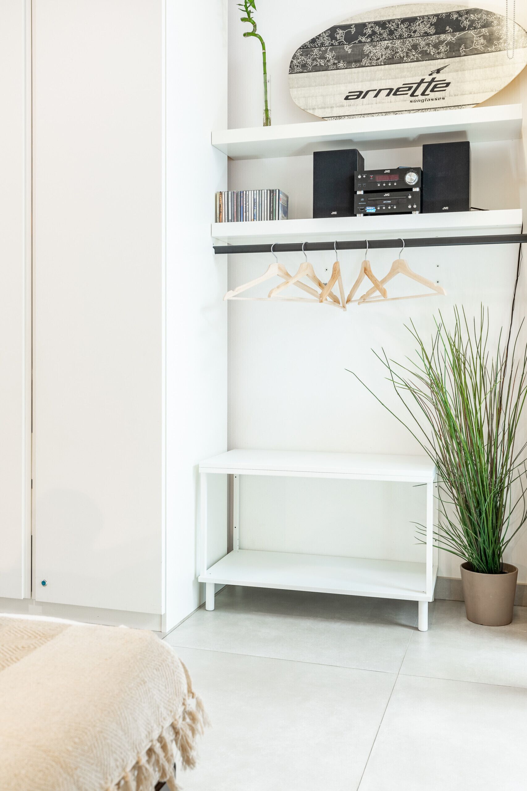A white room with a white shelf holding a plant, a skateboard, and a speaker.
