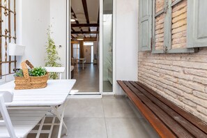 A narrow hallway with a white table and bench, a wicker basket with flowers, and a bamboo plant.