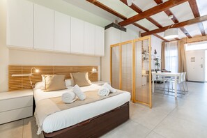 A modern bedroom with a large bed, wooden headboard, and a separate seating area with a table and chairs.