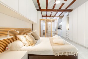 A modern bedroom with a wooden headboard, a large bed with white bedding, a bedside table with a lamp, and a walk-in closet with white cabinets.