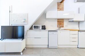 A modern kitchen with white cabinetry, a microwave, a dishwasher, and a TV on a stand.
