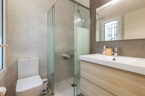 A modern bathroom with a glass-enclosed shower, a white toilet, and a beige vanity with a mirror.