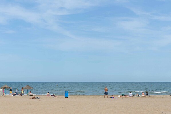 A beach with umbrellas, lounge chairs, and people relaxing.