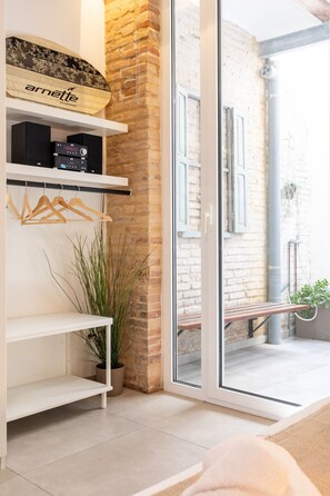 A modern interior with a brick wall, a glass door leading outside, and a shelf with a plant and a wooden hanger.