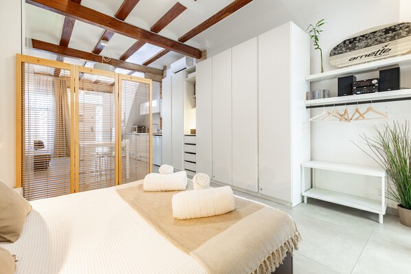 Une chambre à coucher avec un lit, deux serviettes enroulées, une armoire, une étagère avec du matériel audio et une plante en pot.