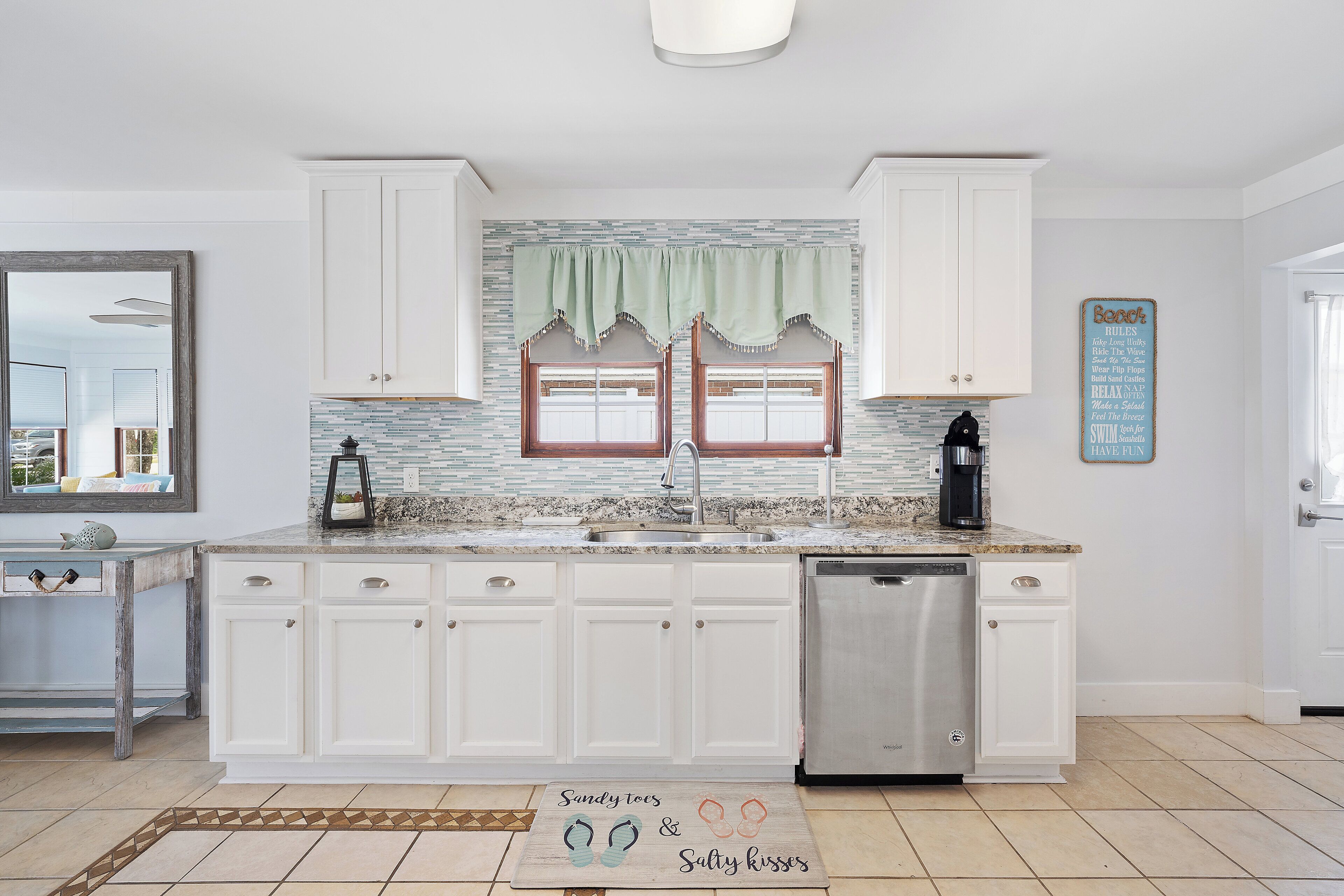 A kitchen with white cabinets, a granite countertop, a dishwasher, and a window with a green valance.