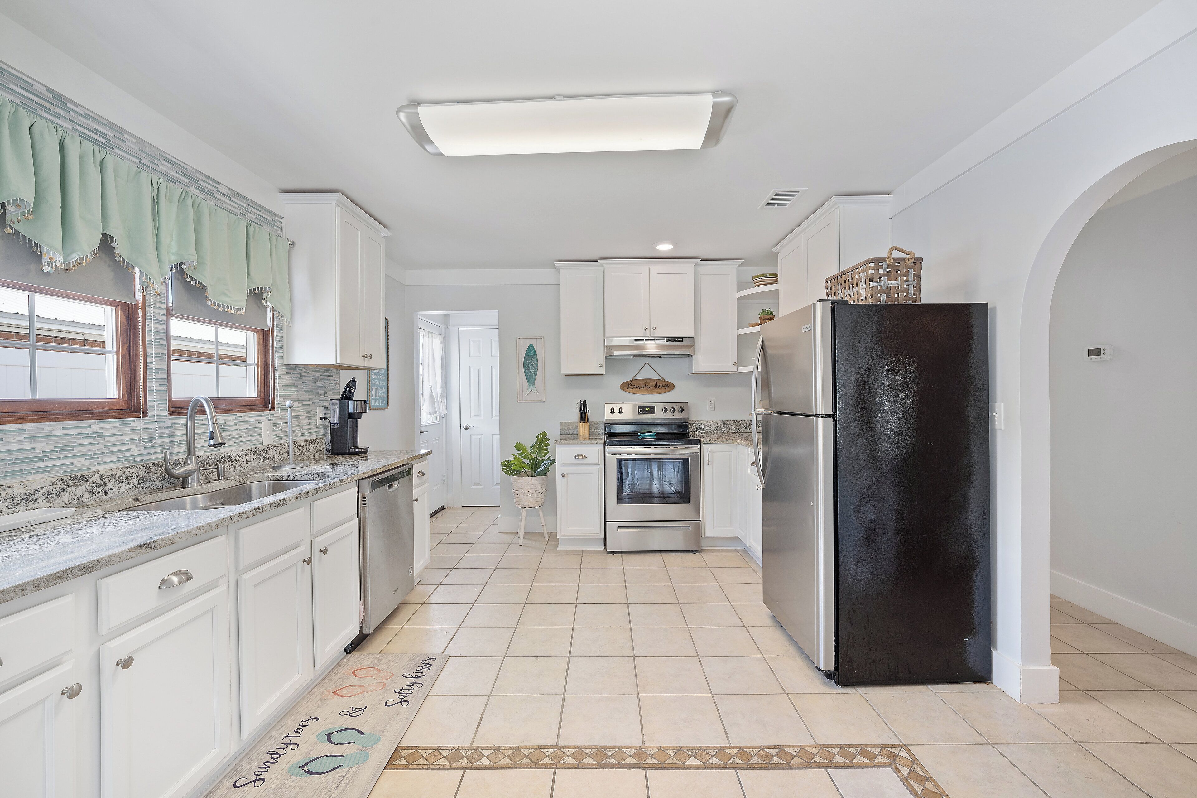 A kitchen with white cabinets, a black refrigerator, a stove, and a sink.