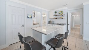A modern kitchen with a central island, bar stools, and a microwave. - Sand and Ocean Lovers Beaach Home! (Panama City Beach)
