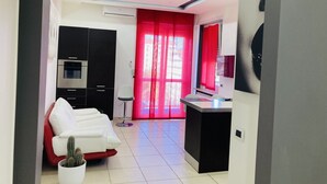 Una sala moderna con un sofá blanco, un sillón rojo y una pequeña planta en maceta.