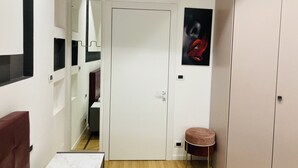 Una habitación con una puerta blanca, una pequeña mesa redonda, una silla roja y un armario.