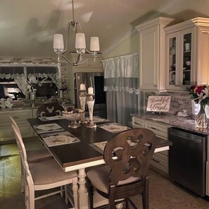 Enjoy meals in this beautifully set dining area with a long table for four, a chandelier, and a floral arrangement.