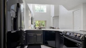 Una cocina moderna con armarios oscuros, horno integrado y un ventanal que proporciona luz natural.