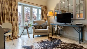 Una sala de estar con un sofá, un televisor, una mesa con una lámpara y un ventanal con cortinas.