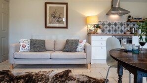 Una sala de estar acogedora con sofá, mesa de comedor y zona de cocina con estufa y salpicadero de azulejos.